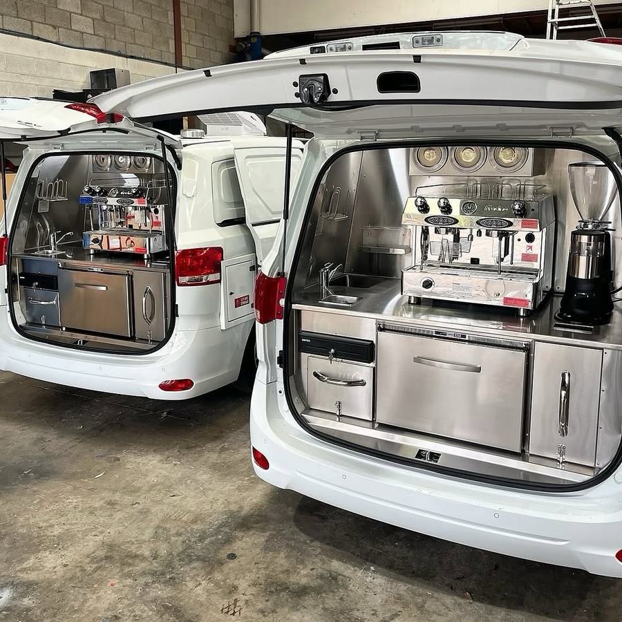 A van with its rear doors open, espresso machine and grinder set up across the tailgate.