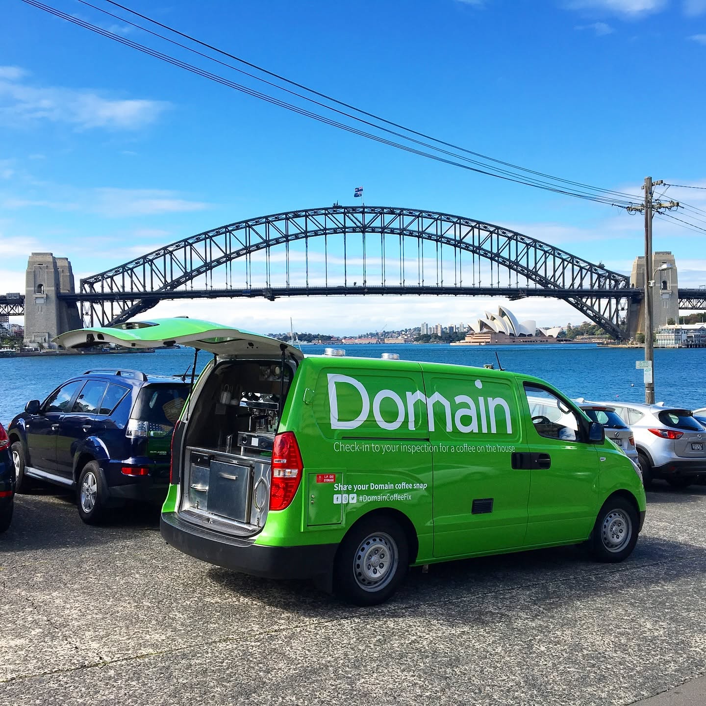 A green Domain coffee van serving with the Sydney Harbour Bridge and Opera House behind it.