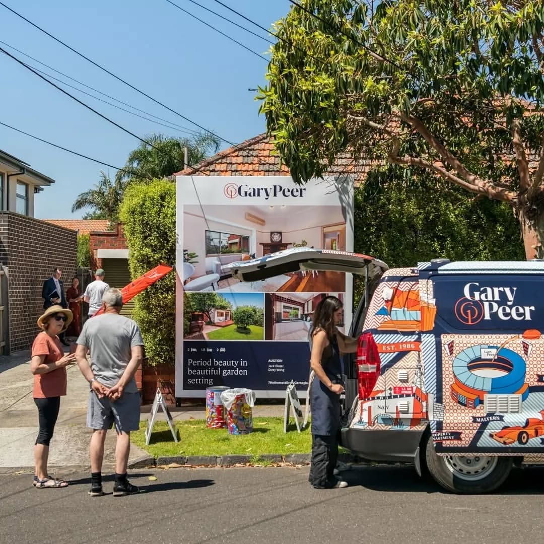 A patterned Gary Peer coffee van serving buyers on a suburban nature strip beside an auction board.