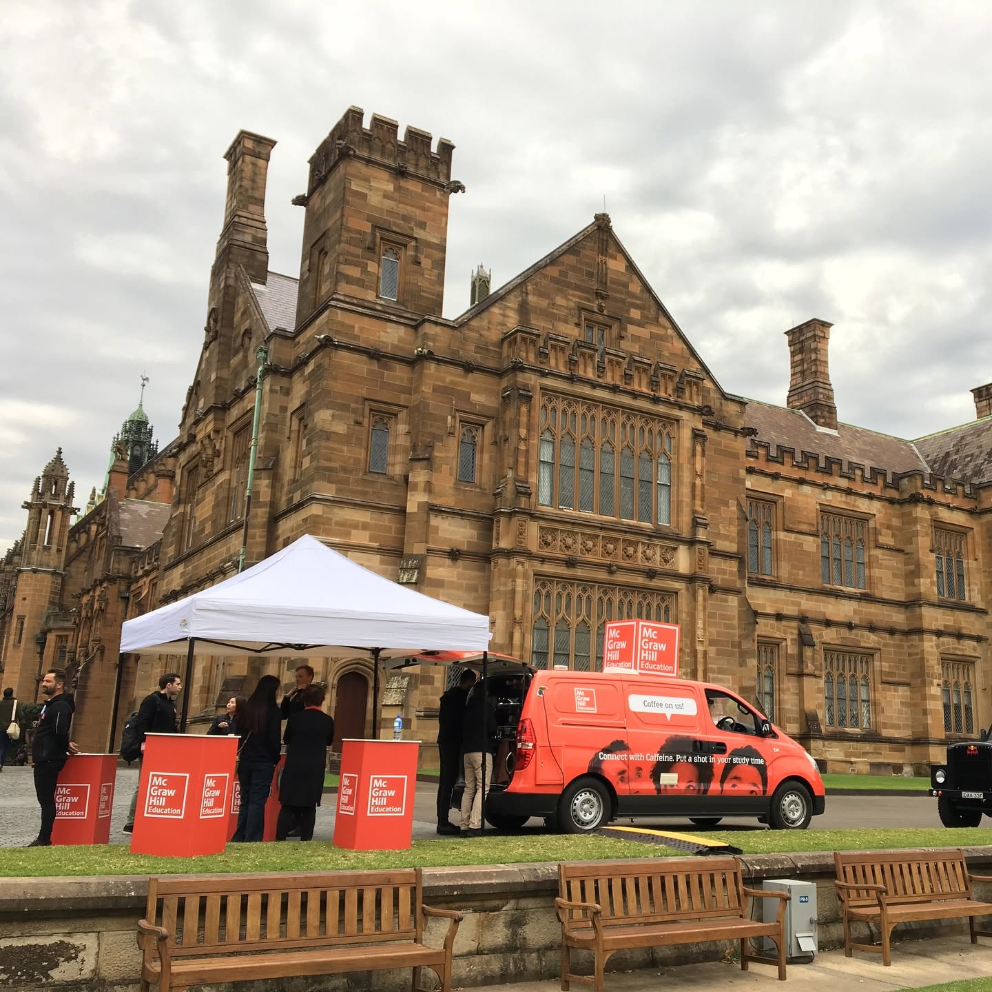 A red coffee van and marquee set up on the lawn in front of the sandstone quadrangle at Sydney University.