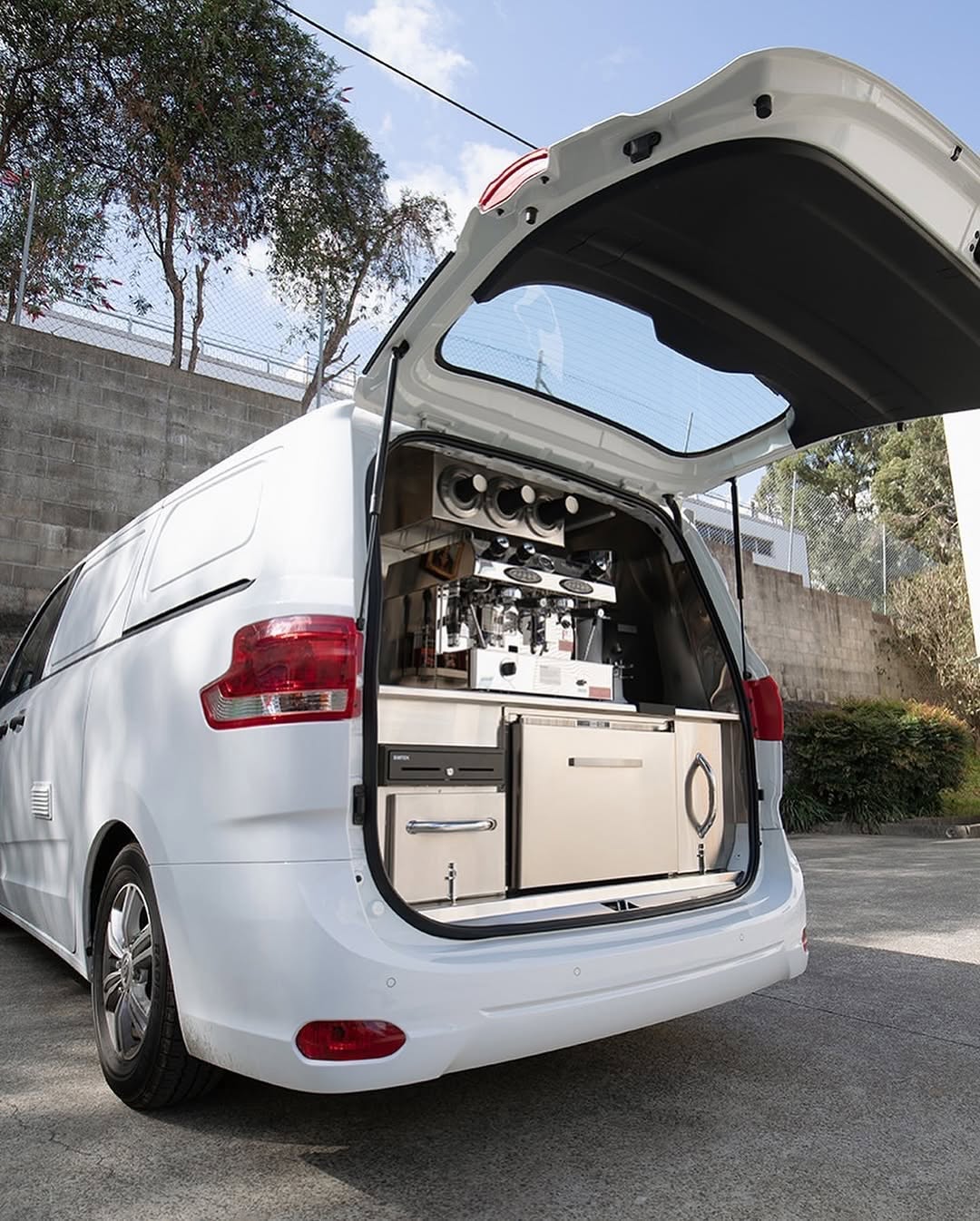 A white LDV G10 with the rear hatch raised over a stainless coffee bench and espresso machine.