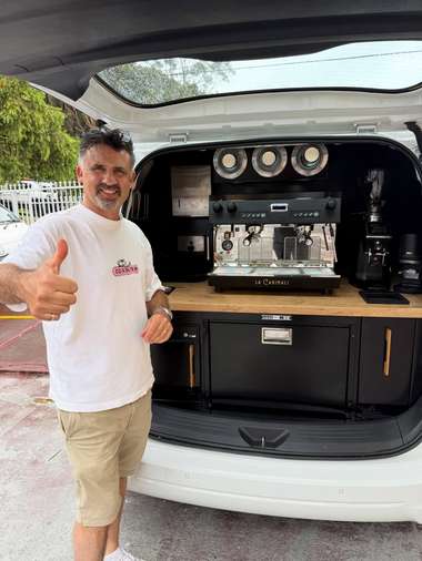 An operator giving a thumbs up in front of the open canopy of his coffee van.
