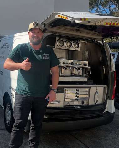 An operator in a green polo giving a thumbs up beside the open rear of his coffee van.
