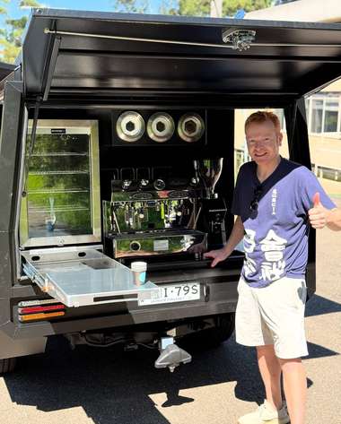 An operator standing beside a dark coffee van with the servery drawer slid out.