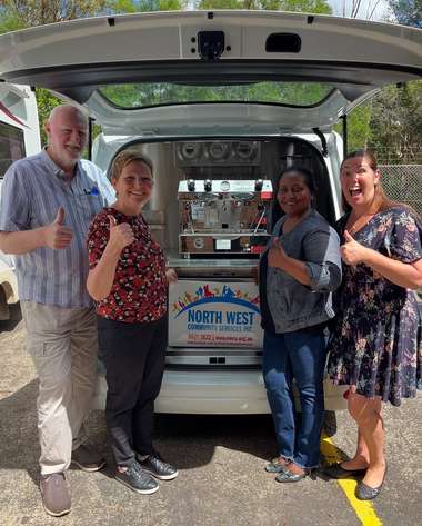 Four people standing together beside a North West coffee van with the rear hatch raised over the machine.