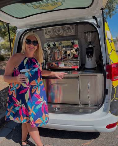 An operator in a bright patterned dress standing at the servery of her coffee van.