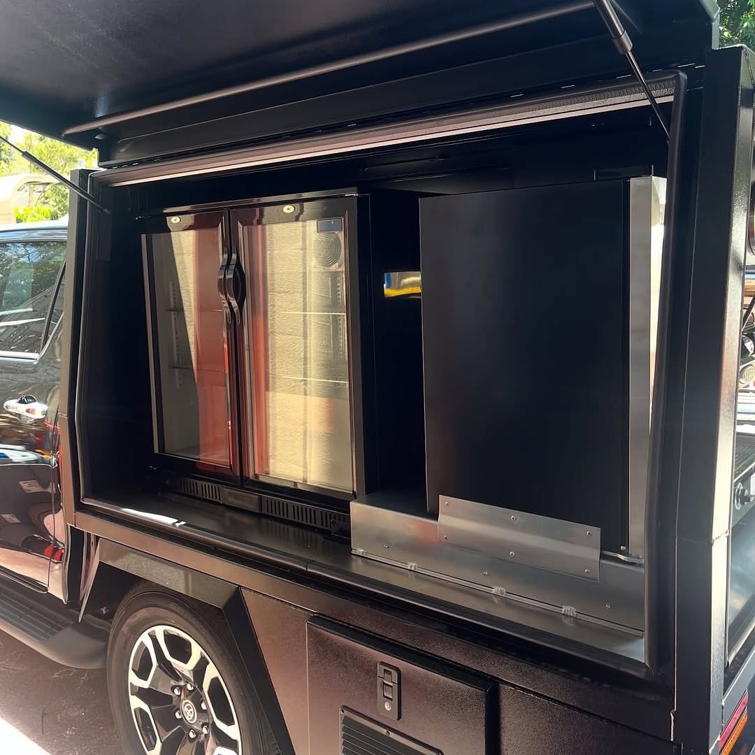 Glass-door fridge and drawer storage in a black canopy