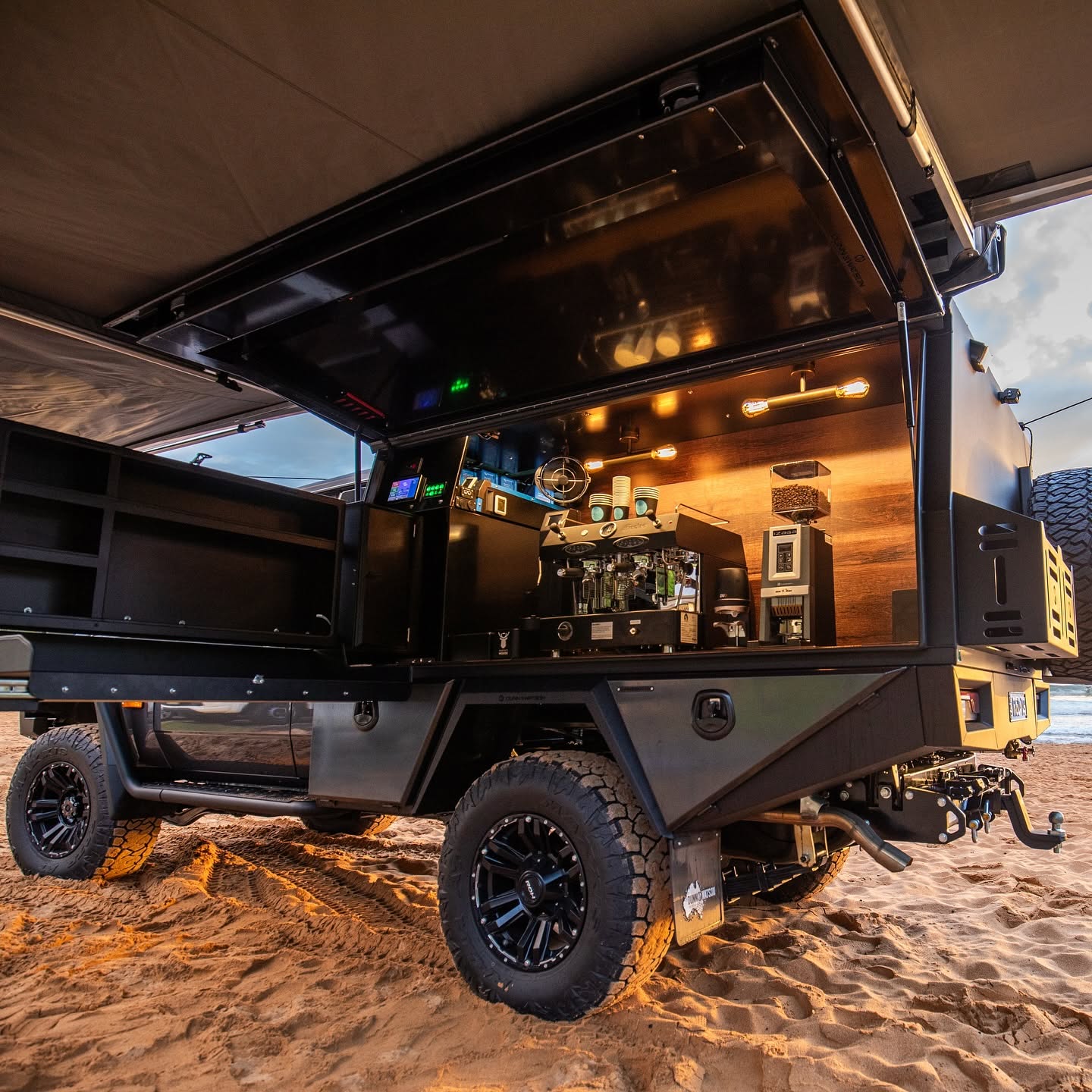 Off-road tourer ute with coffee canopy, on a beach at dusk