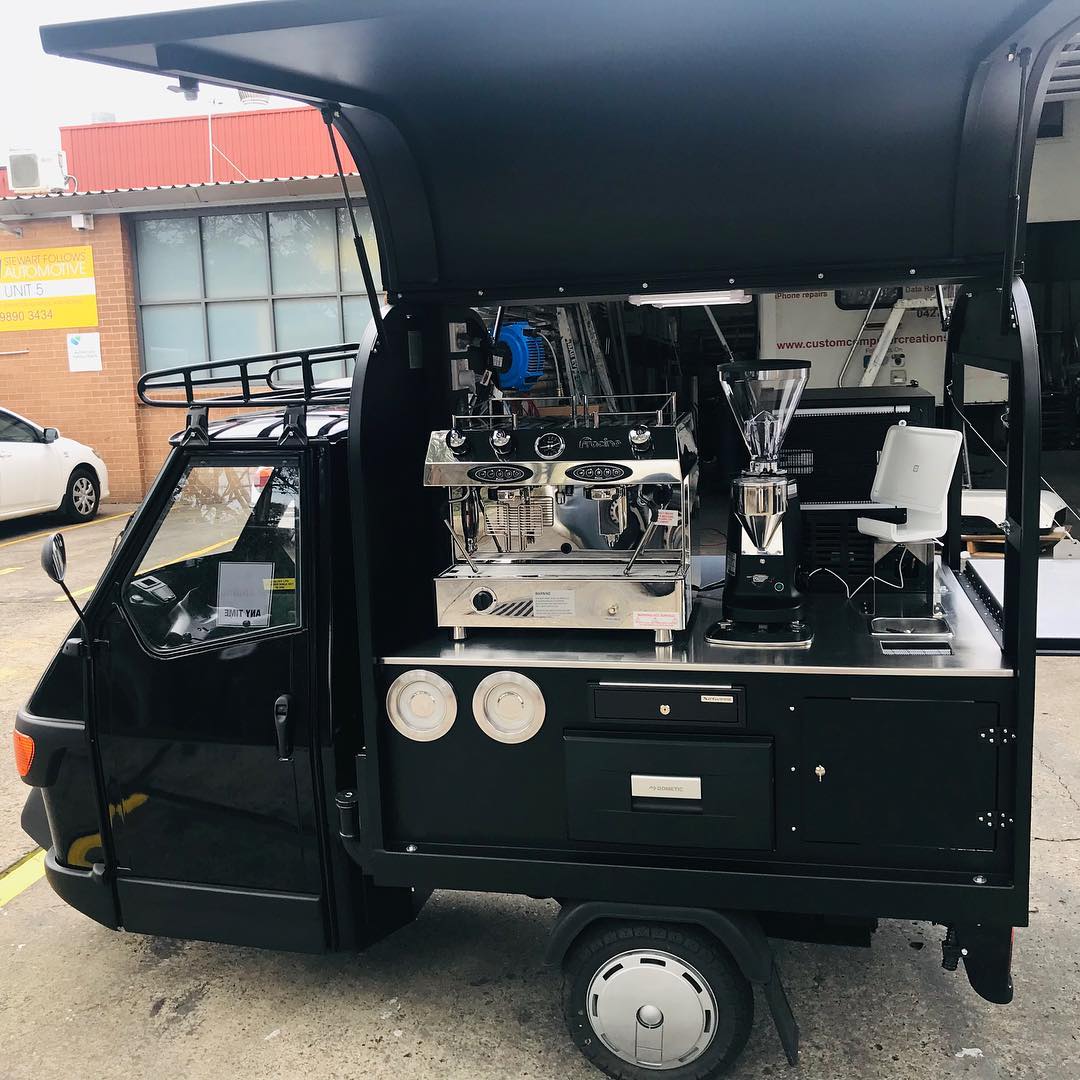 Black Piaggio Ape coffee van, canopy up, espresso machine on the tray