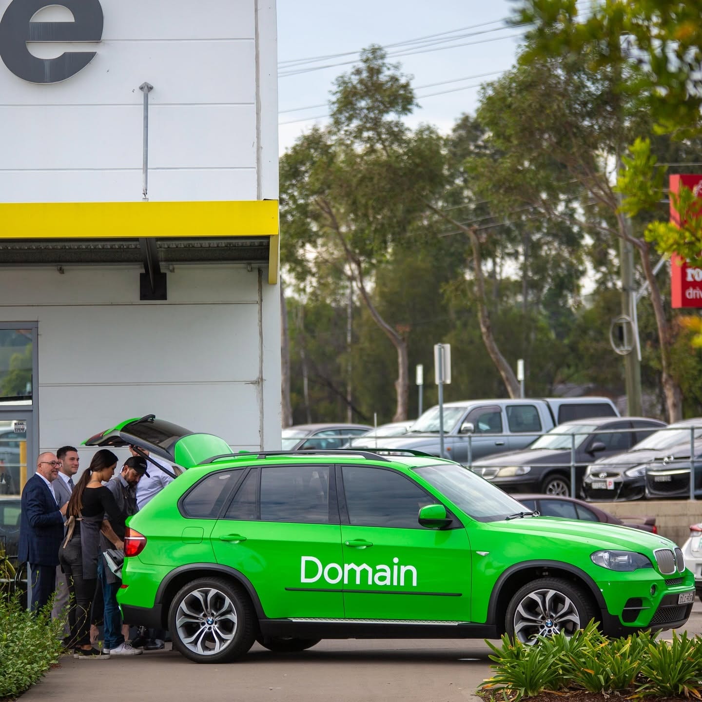 The green Domain X5 outside a building with a small queue being served from the open boot.
